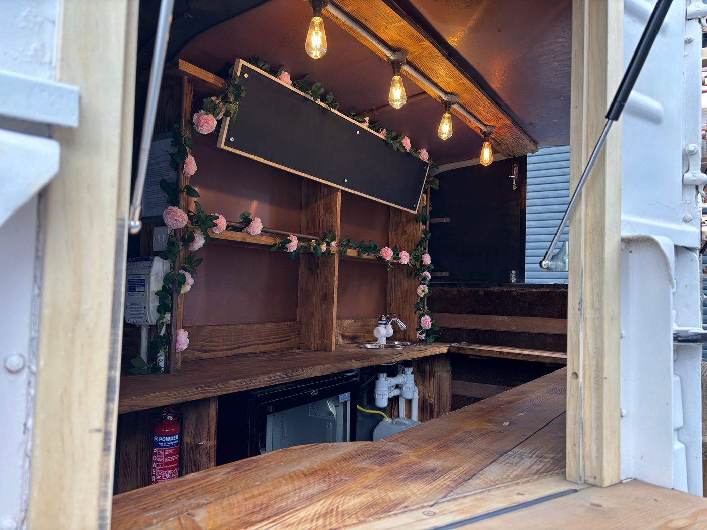 Inside the horsebox bar: chalkboard, rose garland, Edison bulbs and a rustic wooden counter