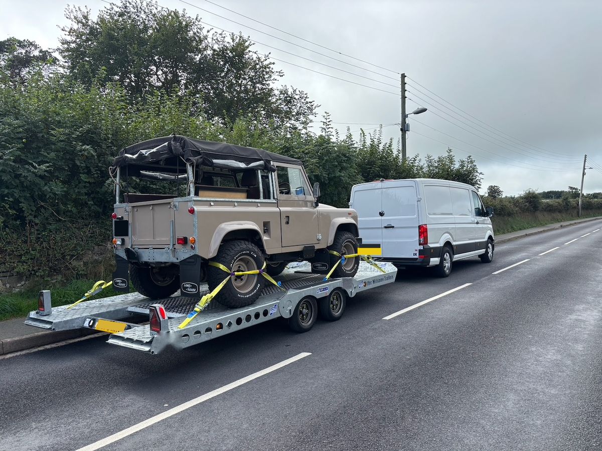 Classic Land Rover Defender strapped onto the transporter, hitched to the van